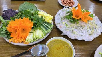 A table with various dishes, including a plate of sliced vegetables, a bowl of soup, and a plate of peanuts.