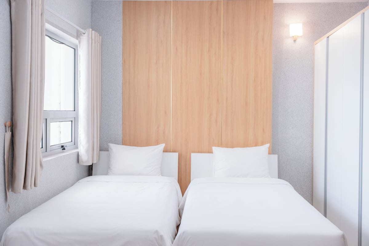 Camera d'albergo con due letti, una testiera in legno, una finestra con tende e una lampada a parete.