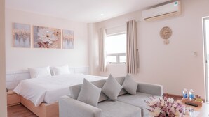 Una camera da letto moderna con un letto, un divano grigio e una finestra con tende. Sono presenti condizionatori fissati al muro e una sveglia.