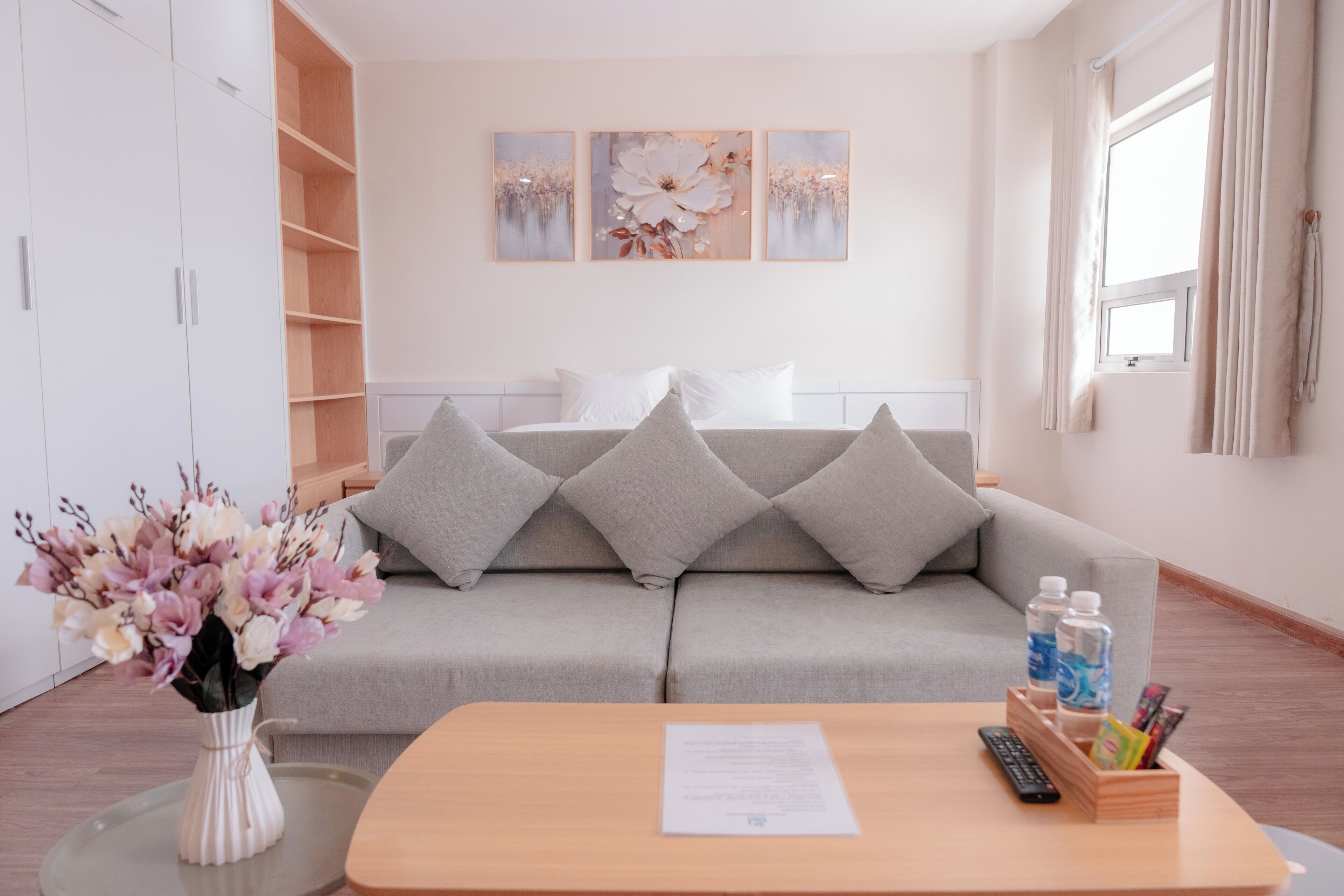 Et moderne hotelværelse med en grå sofa, et træbord, en vase med blomster og en seng med grå puder.