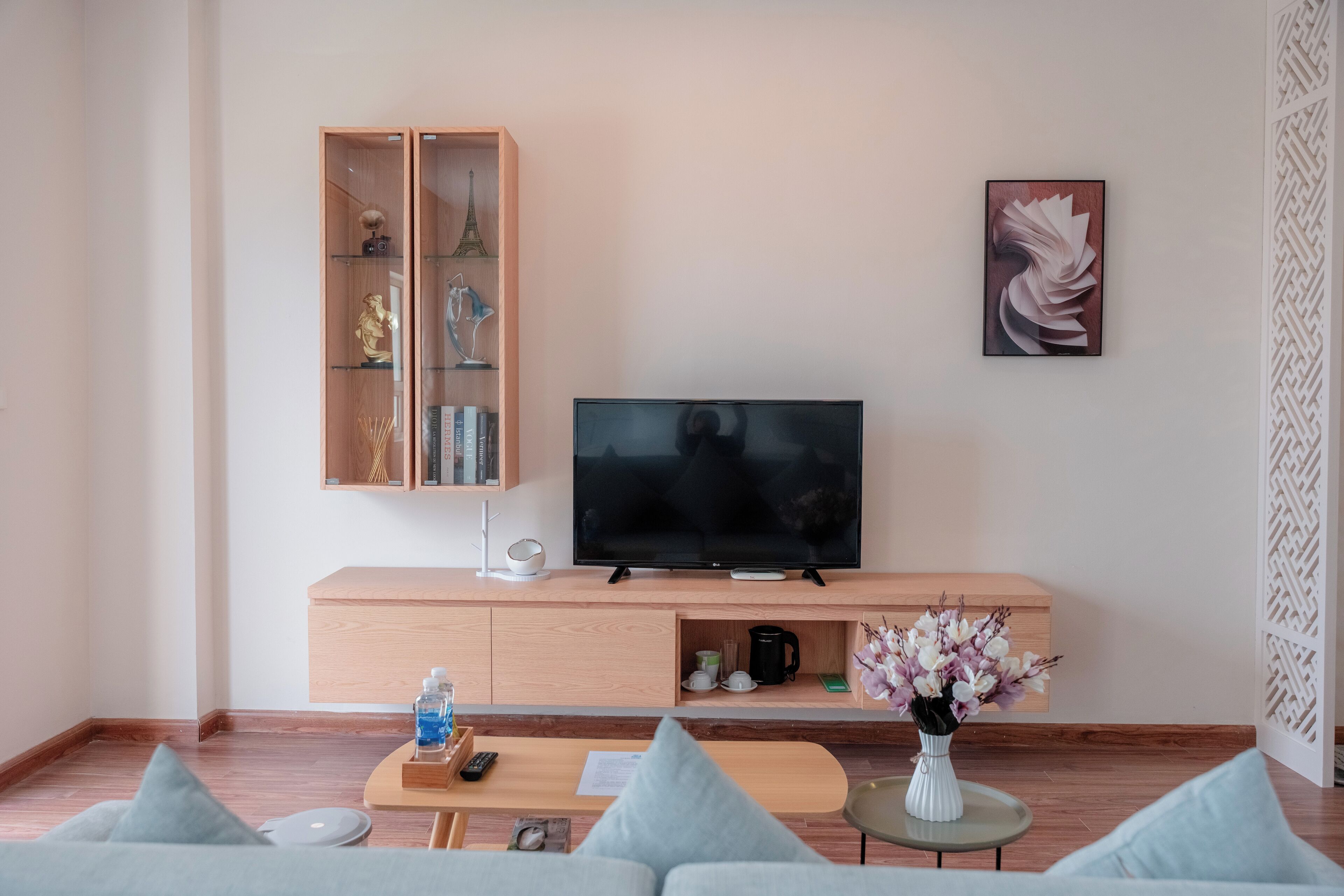 En moderne stue med et fladskærms-TV på et træpanel, kaffemaskine og en vase med blomster.