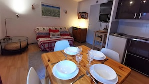 Un salon chaleureux avec un canapé, une table à manger pour deux personnes et un coin cuisine équipé d’une cuisinière et d’un four à micro-ondes.