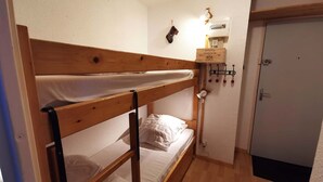 Une petite pièce, de taille modeste, comprenant un lit superposé, une table de chevet avec une lampe, une petite étagère avec une boîte et une porte.