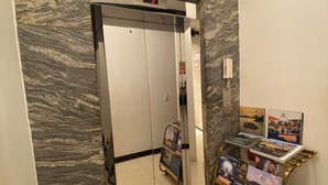 An elevator with a marble wall design, a digital display, and a small trash bin to the left.