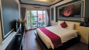 A modern hotel room with a large bed, a flat-screen TV, a desk, and a balcony with a view of buildings.
