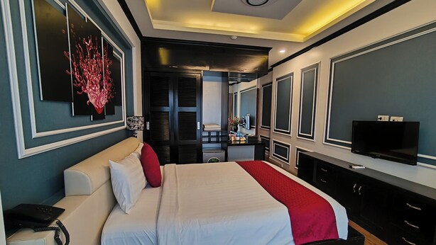A modern hotel room with a large bed, a TV, a desk, and a bathroom visible through an open door.