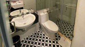 A bathroom with a black and white patterned floor, a glass-enclosed shower, two sinks, and a toilet.