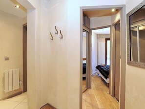 Een smalle gang met een radiator, een deur die naar een slaapkamer leidt, en een spiegel aan de rechtermuur.