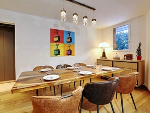Een eethoek met een houten tafel voor zes personen, omringd door lederen stoelen. Aan de muur hangt een kleurrijk kunstwerk, en op een bijzettafeltje staat een lamp.