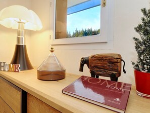 Een houten tafel met een lamp, een decoratieve glazen vaas, een boek met de titel 'HOME' en een potplant.