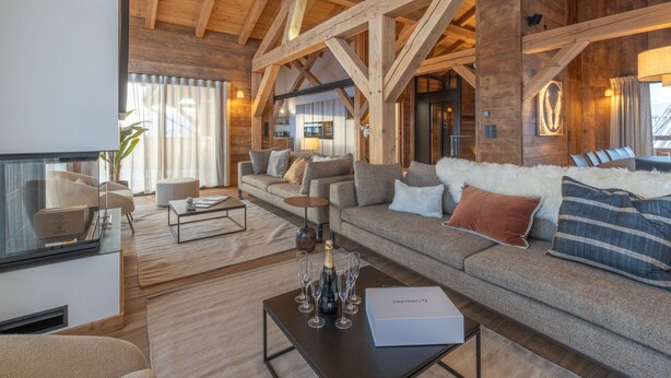 Ein großzügiger Wohnbereich mit hoher Holzbalkendecke, einer Sofagarnitur, einem Couchtisch und einem Fernseher.