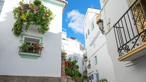 A narrow street with white buildings, green window frames, and balconies with potted plants. - Casa Nobleza in C Mpeta (Còmpeta)