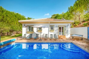 Una casa con piscina, mobiliario exterior y vista a árboles.