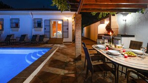 A poolside dining area with a table set for two, a brick wall, and a wooden pergola. - Casa Nobleza in C Mpeta (Còmpeta)