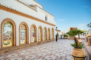 A courtyard with a tiled floor, white building with arched windows, and a person walking. - Casa Nobleza in C Mpeta (Còmpeta)