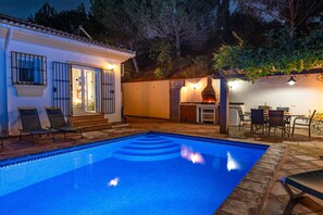 Una piscina con escalones de acceso, rodeada de sillas de descanso y una zona de barbacoa.