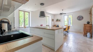 A modern kitchen with a central island, a dining area with chairs, and a view of greenery outside.