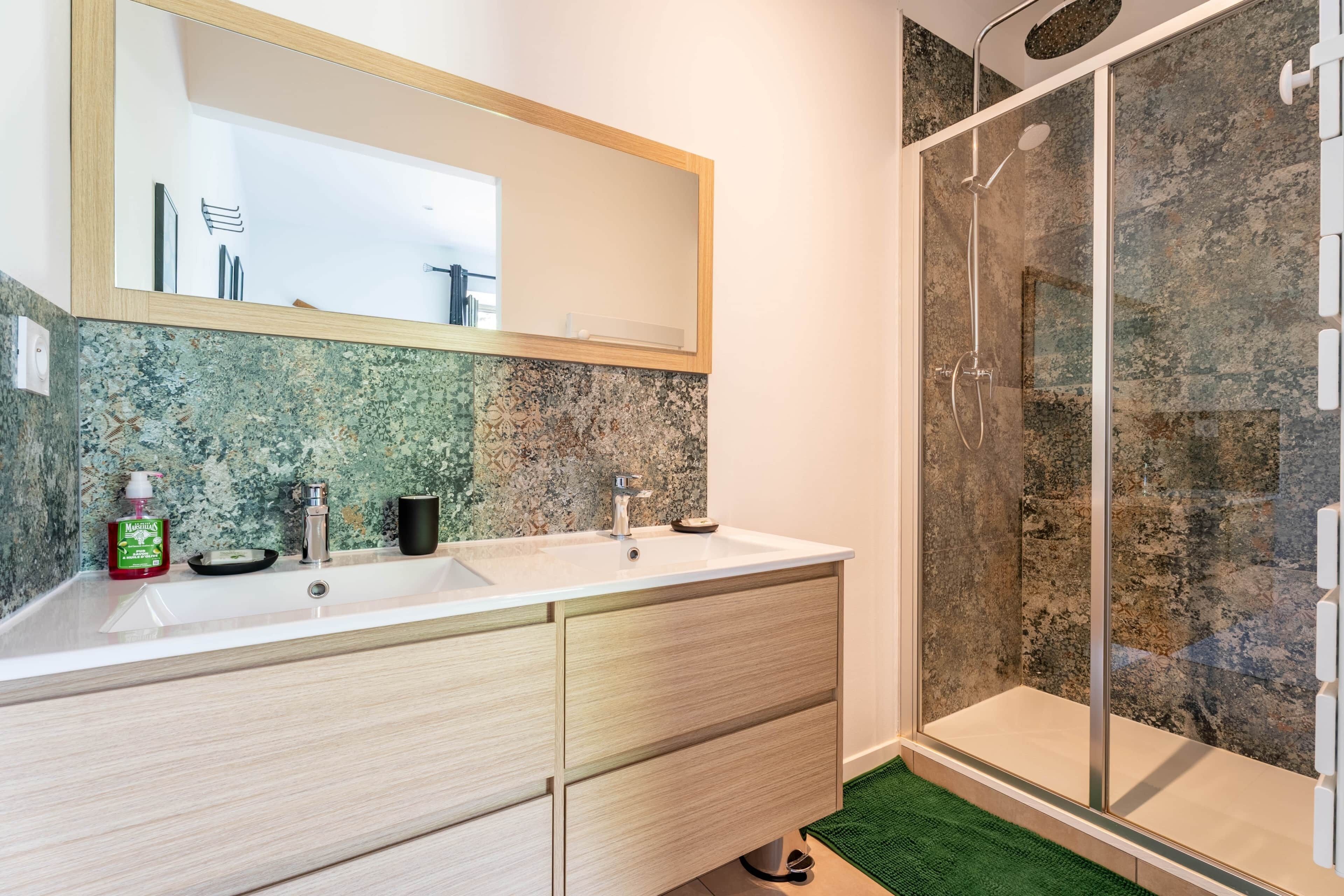 Een badkamer met twee wasbakken, een spiegel en een douchehoek.