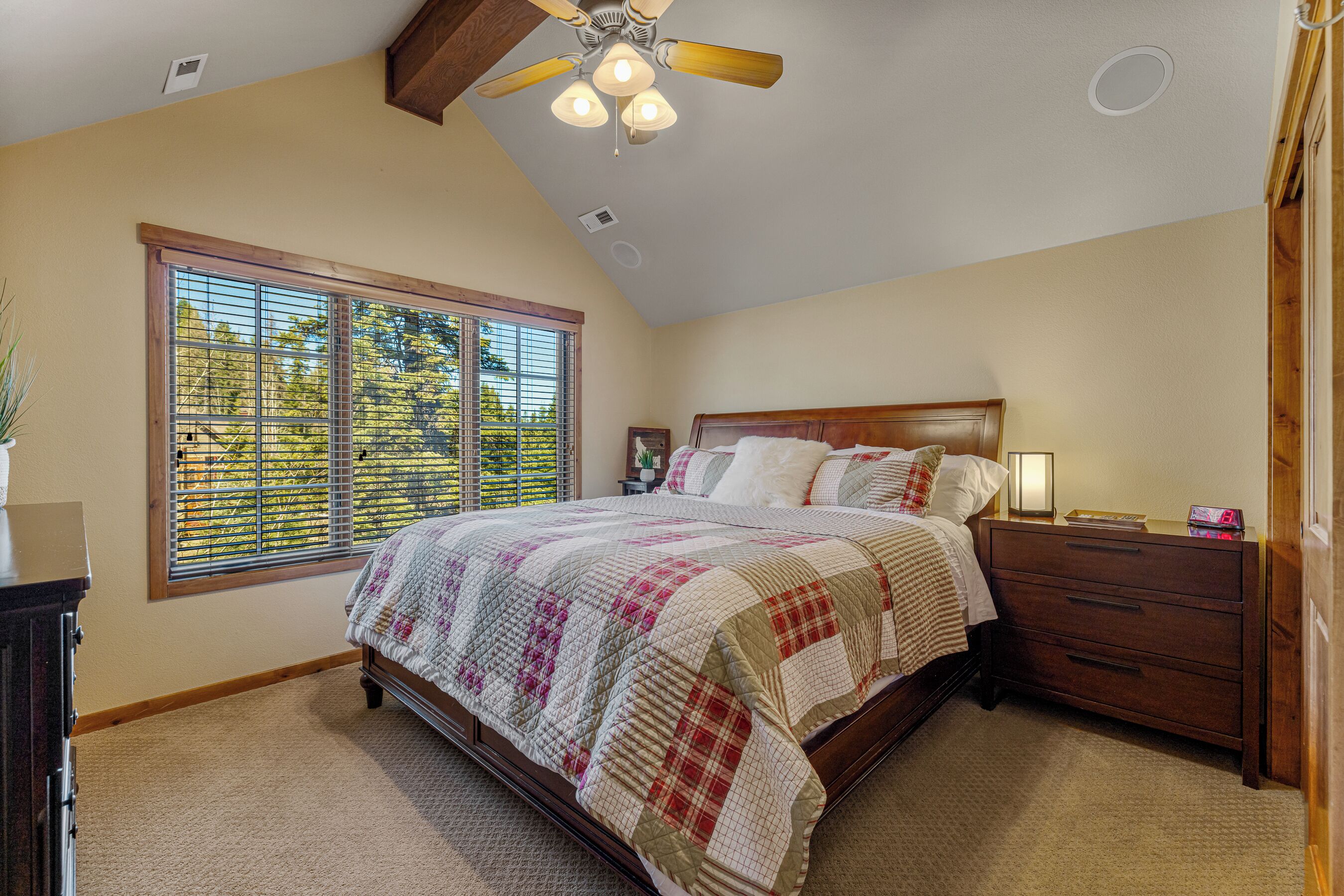 A bedroom with a large window, a bed with a quilt, a nightstand, and a wooden headboard.