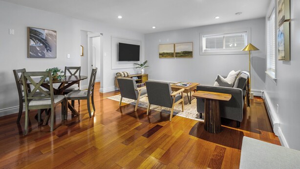 A spacious living room with hardwood flooring, a dining area with wooden chairs, a sofa, and a coffee table. - Forest House 1 Bdrm QV Lake View Parking (St. John's)
