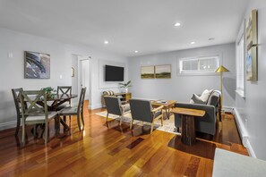 Un salon spacieux doté d’un parquet en bois, un coin repas avec des chaises en bois, un canapé et une table basse.