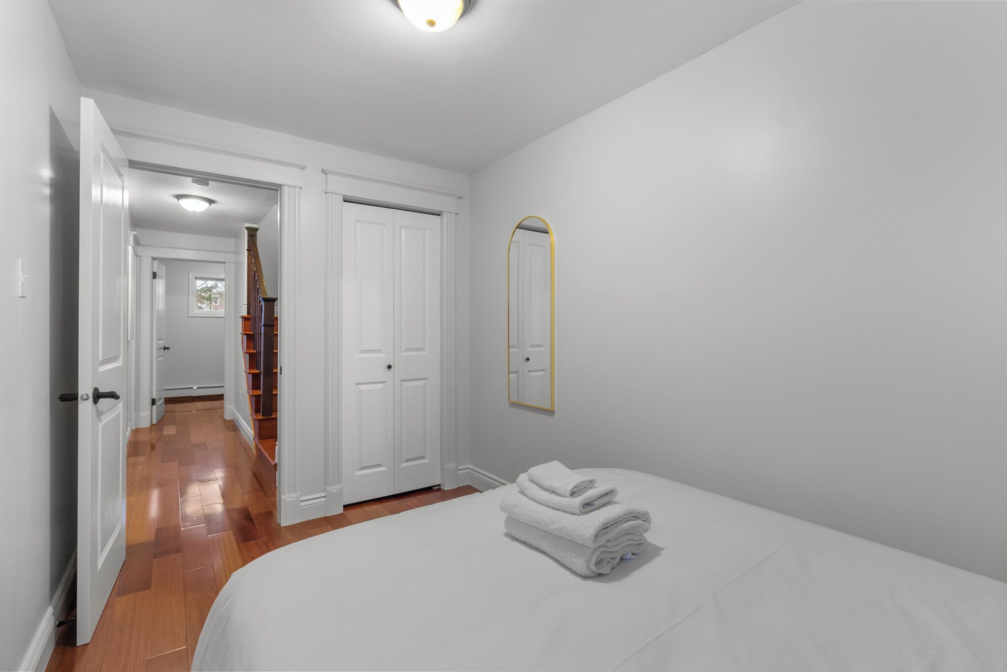 A bedroom with a bed, a stack of towels, a mirror, and a door leading to a hallway.