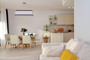 Una sala de estar moderna con comedor, una cocina al fondo y un amplio ventanal.