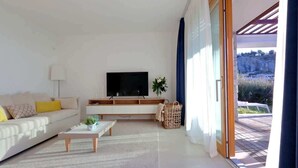 Ein modernes Wohnzimmer mit Sofa, Couchtisch, Fernseher und Blick durch eine Schiebetür auf eine Terrassenanlage.
