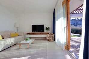 Una sala de estar moderna con un sofá, una mesa de centro, televisor y vistas a una terraza exterior.