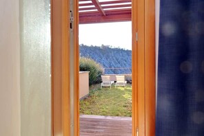 Una porta aperta che dà su un patio con tavolo e sedie, un pavimento in legno e vista su una collina.