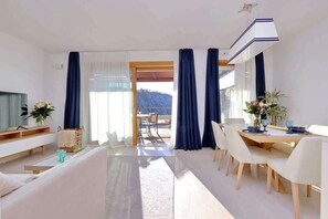 Un soggiorno moderno con divano, tavolo da pranzo, sedie, televisore e un balcone con tende.