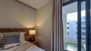 Une chambre d’hôtel avec un grand lit, une tête de lit en bois, une lampe de chevet et une vue sur un immeuble par la fenêtre.