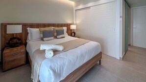 A modern hotel room with a large bed, wooden headboard, bedside lamps, and a walk-in closet.