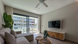 A modern living room with a sofa, a coffee table, a TV, and a balcony with a view of a building.