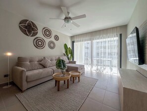 Una sala moderna con un sofá color beige, un ventilador de techo y decoración en la pared.