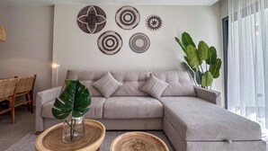 A modern living room with a grey sectional sofa, two wooden side tables, a large green plant, and wall art.