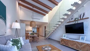 A modern living room with a sofa, coffee table, and TV. There is a staircase leading to an upper level. - Stunning Penthouse located at Cocotal Golf Course (Punta Cana)