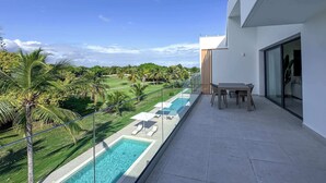 A modern balcony with a glass railing overlooking a swimming pool and lush greenery. - Stunning Penthouse located at Cocotal Golf Course (Punta Cana)
