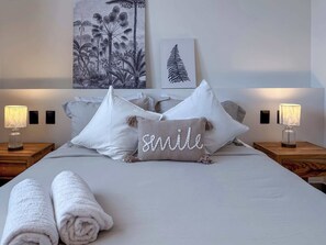 A neatly made bed with white linens, two bedside lamps, and a pillow with the word "smile" on it.