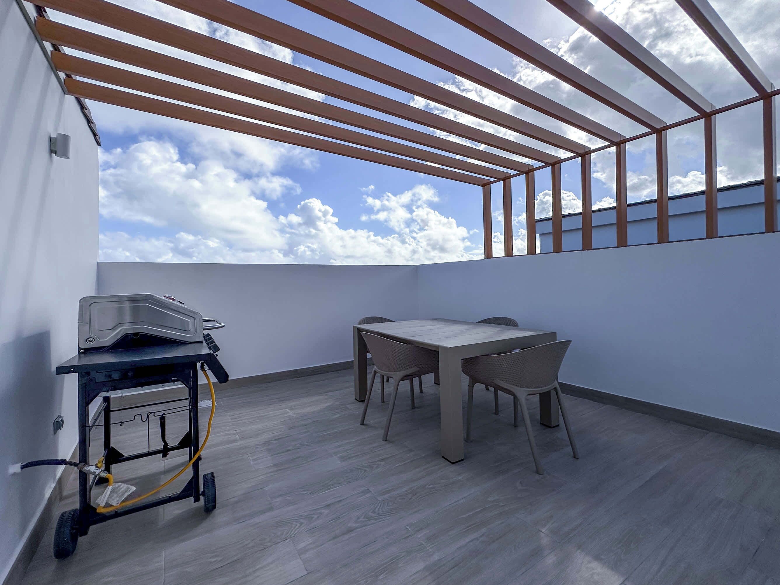 A balcony with a table and chairs, a cart, and a view of the sky.