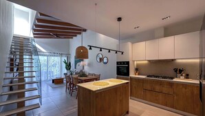 A modern kitchen with wooden cabinetry, a central island, and a dining area with a staircase. - Stunning Penthouse located at Cocotal Golf Course (Punta Cana)