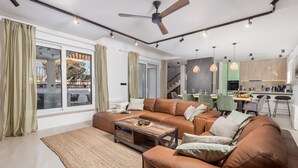 A modern living room with a brown leather sofa, a wooden coffee table, and a large window with curtains. - Cozy home in Skrip with WiFi (Skrip)