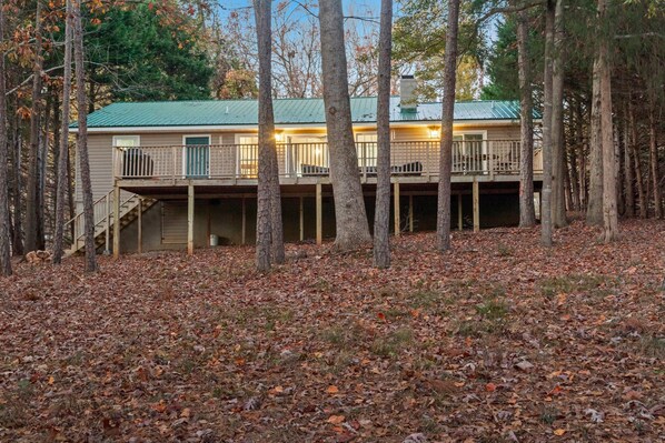 A two-story cabin with a green roof, surrounded by trees and covered in fallen leaves.