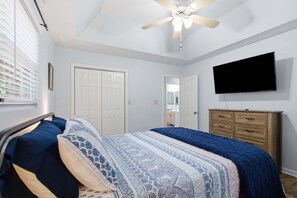 Un dormitorio con cama, televisor, ventilador de techo y cómoda.