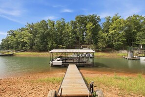 A wooden dock leading to a covered boat launch area with a view of a forested riverbank.