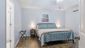 A bedroom with a bed, a ceiling fan, a window with blinds, and a nightstand with a lamp.