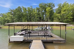 A covered dock with a boat, a small building, and a forested area in the background.