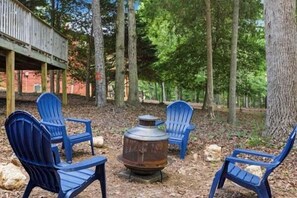 Un área boscosa con un espacio de estar al aire libre rústico, que incluye dos sillas azules y un brasero metálico.