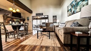 A cozy living room with a wooden floor, a sofa, a coffee table, and a TV mounted on a wooden beam above the fireplace.