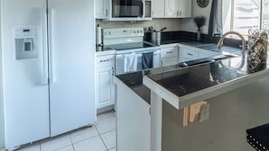 Una cucina compatta con mobili bianchi, un forno a microonde, un piano cottura e un lavello.